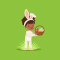 Beautiful little girl with bunny ears and rabbit costume standing with basket full of painted eggs, kid having fun on Royalty Free Stock Photo