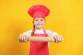 Beautiful little girl chef on a yellow background. The child holds in his hands a wooden rolling pin