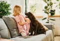 Beautiful little girl, child sitting on couch and playing with purebred dog, brown labrador at home. Comfort and Royalty Free Stock Photo