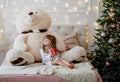 Beautiful little girl in a Christmas room drinking coffee in a bed with large Teddy bear plush toy