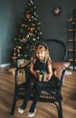 Beautiful little girl with closed eyes and with gift box in hands sitting in chair. Christmas surprise