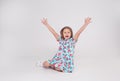 a beautiful little girl in a colorful bright dress laughs and raises her hands up sitting on a white isolated background Royalty Free Stock Photo