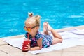 Beautiful little girl, cute toddler with blonde hair in swimwear, sitting at a swimming pool and drinking water melon juice with Royalty Free Stock Photo