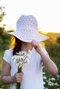 A beautiful little girl with daisies covers her face with a hat Royalty Free Stock Photo