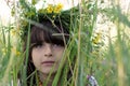 Beautiful little girl with green eyes and a colorful garlang made of wild flowers on her head sits in high green grass on a meadow Royalty Free Stock Photo