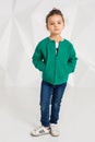 Beautiful little girl in a green jacket and jeans posing in front of camera in studio