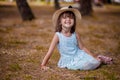 Beautiful little girl in a hat and white dress girl sitting on the lawn and laughing on a beautiful autumn warm day. Royalty Free Stock Photo