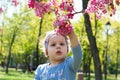 Beautiful little girl with headband in spring day in the park. Close up view of the cute girl reaches for the flower of the trees Royalty Free Stock Photo