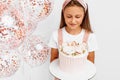 Beautiful little girl holding a beautiful big birthday cake, birthday celebration with balloons, over white background Royalty Free Stock Photo