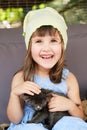 Beautiful little girl in a Light Blue dress holding gray kitten and smiling. A Royalty Free Stock Photo