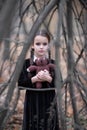 Beautiful little girl with long brunette hair, dressed in black velvet dress walks in fall forest with handmade bear toy.