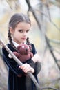 Beautiful little girl with long brunette hair, dressed in black velvet dress walks in fall forest with handmade bear toy.