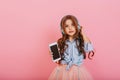 Beautiful little girl with long brunette hair with phone listening to music through blue headphones isolated on pink Royalty Free Stock Photo