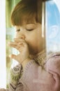 A beautiful little girl looks out the window alone, sad and waiting for her parents. isolation at home. Royalty Free Stock Photo