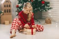 Beautiful little girl opens a gift at home under a kraft paper tree tied with a red ribbon, new year mood. Holiday concept for Royalty Free Stock Photo