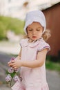 A beautiful little girl in a pink dress holds a branch of lilac flowers. Child in the garden on a background of a wooden fence Royalty Free Stock Photo