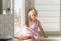 Beautiful little girl in a pink dress sits on the window Royalty Free Stock Photo