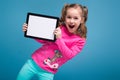 Beautiful little girl in pink shirt with monkey and blue trousers hold empty tablet