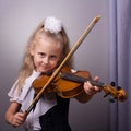 Beautiful little girl playing the violin on bright gray