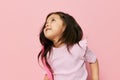 a beautiful little girl of preschool age stands on a pink background in a pink T-shirt and looks thoughtfully away Royalty Free Stock Photo