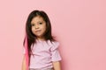 a beautiful little girl of preschool age stands on a pink background in a pink T-shirt and looks thoughtfully away Royalty Free Stock Photo