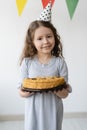 Beautiful little girl princess celebrates a birthday. She stands in a bright room and holds a cake in her hands. On her Royalty Free Stock Photo
