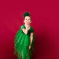 Beautiful little girl princess dancing in luxury green dress isolated on red background. Carnival party with costumes Royalty Free Stock Photo