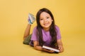 beautiful little girl reads a book while lying. Cute baby teaches lessons on a yellow background