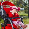 Beautiful little girl in a red jacket on the pram in park