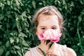 A beautiful little girl with sad eyes is thinking about something and holding a peony flower in her hand by green plants Royalty Free Stock Photo