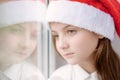 Beautiful little girl in Santa hat dreaming by the window Royalty Free Stock Photo