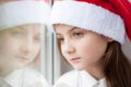 Beautiful little girl in Santa hat dreaming by the window Royalty Free Stock Photo