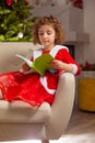 Beautiful little girl sits on the chair next to a nicely decorated Christmas tree Royalty Free Stock Photo