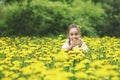 A beautiful little girl sits in a field with yellow dandelions and smiles. Walk in the spring in the city park. Royalty Free Stock Photo