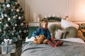 a beautiful little girl is sitting on the bed hugging a plush toy near a decorated Christmas tree Royalty Free Stock Photo