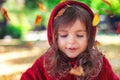 Beautiful little girl as red riding hood playing with fallen leaves at autumn park Royalty Free Stock Photo