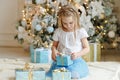 Beautiful little girl sitting near Christmas tree and looking for a gift, a bright interior Royalty Free Stock Photo