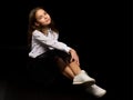 A little girl is sitting in the studio on the floor on a black background. Royalty Free Stock Photo