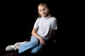 A little girl is sitting in the studio on the floor on a black background. Royalty Free Stock Photo