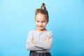 Beautiful little girl smiling, crossed her hands, has a positive expression, standing on blue isolated.