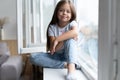 Beautiful little girl watching out the window. Young girl looking from window. Cheerful kid lies at windowsill Royalty Free Stock Photo