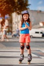 Beautiful little girl stands in roller skates at a city park in the sunshiny summer day. Royalty Free Stock Photo