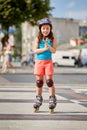 Beautiful little girl stands in roller skates at a city park in the sunshiny summer day. Royalty Free Stock Photo