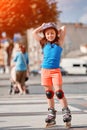 Beautiful little girl stands in roller skates at a city park in the sunshiny summer day.