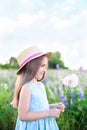 Beautiful little girl in a straw hat and dress holds a dandelion in a flowering field. Nature concept. A smiling girl is playing o Royalty Free Stock Photo