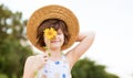 Beautiful little girl in straw hat with fluttering hair hide eye with sunflower flower, walking outdoor in summer Royalty Free Stock Photo