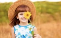 Beautiful little girl in straw hat with fluttering hair hide eye with sunflower flower, walking outdoor in summer Royalty Free Stock Photo