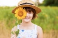 Beautiful little girl in straw hat with fluttering hair hide eye with sunflower flower, walking outdoor in summer Royalty Free Stock Photo