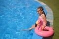 A beautiful little girl in a striped pink swimsuit is sitting on the edge of pool with a flamingo-shaped swimming circle. Royalty Free Stock Photo