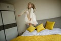 Beautiful little girl in stylish dress jumping on the bed with white blanket at home. Stay at home during coronavirus Royalty Free Stock Photo